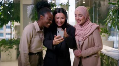 Mutlu çok ırklı kızlar iş arkadaşları, neşeli iş arkadaşları, Afrikalı Müslüman Asyalı kadınlar, cep telefonlarından iyi haberler alıyor. İyi haberler, zaferler.