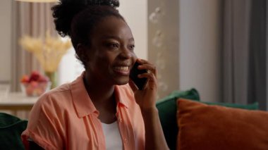 Mutlu gülen müşteri Afrikalı Amerikalı etnik iş kadını kadın model kadın ev sahibi ev sahibi arkadaşlarıyla konuşan cep telefonu konuşan akıllı telefon evde dedikodu yapan