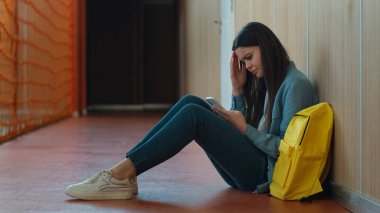 Üzücü bir başarısızlık. Düşünceli kız öğrenci kız öğrenci eğitiminin okul koridorunda cep telefonu akıllı telefonu sosyal medya uygulaması kullanarak oturduğunu vurgula.