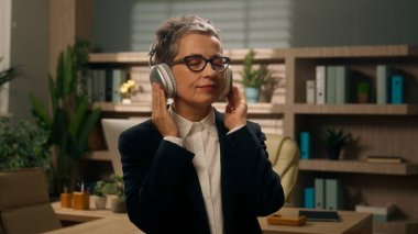 Rahatlatıcı iş, özgürlüğü durdurur Kafkasyalı kıdemli iş kadını orta yaşlı yetişkin kadın işkadını ofiste kablosuz kulaklıklarla müzik dinleyen yetişkin kadın işveren müzik dinlemenin tadını çıkar