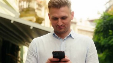 Beyaz adam gülümseyen turist şehirde cep telefonu aygıtı kullanıyor. Erkek işadamı, akıllı telefon uygulaması, internet bağlantıları, açık havada tatil biletleri alıyor.