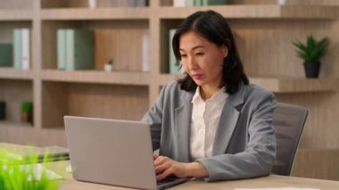Asyalı kadın iş kadını mutlu girişimci bayan ofis çalışanı Japon Koreli kız online iş yeri bilgisayarında neşeli bir kutlama laptopu kazanmayı kutluyor kumar parası iş başarısı