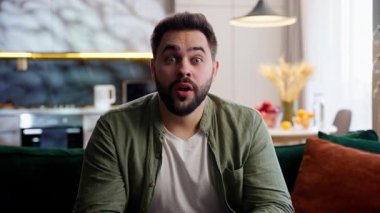 Kafası karışmış Kafkasyalı iş adamı erkek iş adamı ev sahibi model kameraya bakıp şoke oldum. Vay canına, el kol hareketi yapan eller ev içinde inanılmaz haberler veriyor.