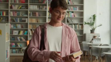 Genç adam, elinde kitap tutarak mutlu bir şekilde gülümsüyor. Kitap satın alıyor. Lisedeki kitapçıda okumaya hazırlanıyor.