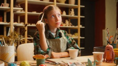 Kafkasyalı küçük kız, ergen kız, çömlekçi kız, çömlekçi, çömlekçi, elinde kil şekilli araç gereçler, el yapımı sanat eserleri atölyesinden ilham aldığını düşünüyor.