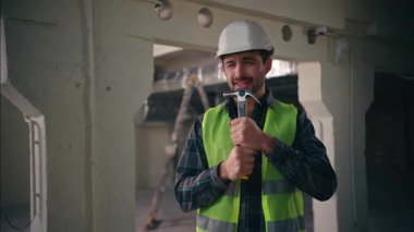 Neşeli, aktif, beyaz bir adam elinde çekiç tutarken mikrofon kullanıp şarkı söylüyor. Müzikten zevk alıyor. Erkek, mimar, müteahhit, inşaat işçisi inşaatında çalışıyor.