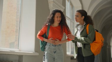 İki öğrenci kız Latin kız. Üniversite koridorunda yürüyen Latin bayan arkadaş. Konuşan kadın. Karın ağrısı çekiyor.