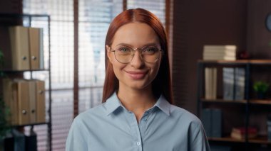 Dostane gülümseyen, arkadaş canlısı, başarılı, beyaz, kadın, iş kadını, gözlüklü, gözlüklü, gözlüklü, ofiste kameraya bakan kadın.