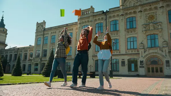 Üç çok ırklı öğrenci kız Afrikalı Amerikalı kadın, beyaz kadın erkek, üniversiteden erkek, liseden ayrılıp kitap atarak eğitim tatilini kutluyor.