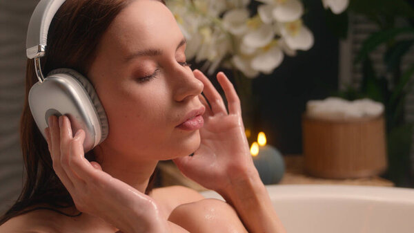 Женщина слушает музыку в беспроводных наушниках слушать аудио звуковая песня в домашней ванной комнате расслабляющий отдых насладиться красотой рутины Кавказская девушка женщина в ванной ванна горячая вода гигиена процедуры