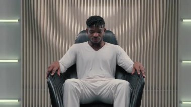 Futuristik kendine güvenen ciddi oyun programcısı Afrikalı Amerikalı erkek adam koltukta oturan fütürizm modern oda stüdyosu koltukta 3D bilgisayar grafikleri ve yapay zeka ağı konseptine bakıyor.