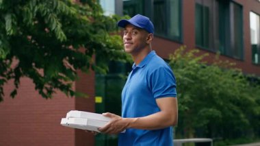 Gülümseyen erkek kafe pizzacısı. Afro-Amerikan erkek kurye. Elinde karton kutu pizza, fast food paketi.