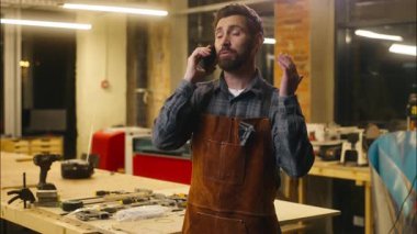 Neşeli Kafkasyalı adam ahşap ustası konuşan cep telefonu tasarımcısı müşteri marangozuyla cep telefonu tamircisi atölye marangozluğu sanatında çalışan adamla konuşuyor.