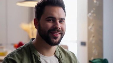 Mutlu gülümseyen, Avrupalı, sakallı, neşeli adam, iş adamı, başarılı ev sahibi, müşterisi, başını çeviren kamera tebessümü, oturma odasındaki portre fotoğrafına bakıyor.