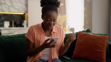 Gülen mutlu Afrikalı Amerikalı kadın etnik iş kadını gülümsemesi kazanan cep telefonu zaferini kutlayan akıllı telefon zaferini kazanan evde tezahürat çığlığı atan başarı çığlığı atan