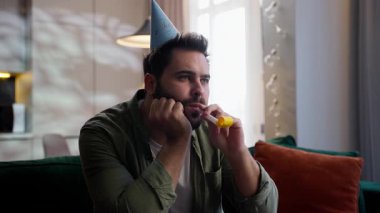 Yalnız, üzgün, Kafkasyalı, erkek, iş adamı, hayal kırıklığına uğramış, ev sahibi, şenlikli şapkalı, ıslık çalan, tek başına, doğum günü partisi arkadaşlığı kutlayan, evde oturma odasında oturan adam.