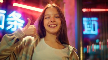 Gülümseyen Kafkasyalı Asyalı küçük çocuk başparmağını kaldıran çocuk şehir kızına katılıyor olumlu jest evet tavsiye eden neon kız geribildirim kızı başarılı işaret gecesi