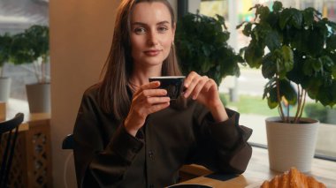 Mutlu gülümseyen, Kafkasyalı, rahat, beyaz kadın, iş kadını, kafeterya restoranındaki kafede, aromalı kahve içen, kahvaltı içen, kameraya gülümseyen.