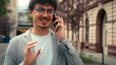 Gülümseyen iş adamı, mutlu İspanyol adam şehir sokaklarında dolaşıyor, dışarı çıkıyor cep telefonundan memnun bir şekilde konuşuyor iletişim kuruyor.