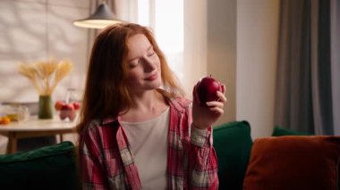 Evde gülümseyen diş hekiminin portresi. Oturma odasında elinde kırmızı elma meyvesi tutan beyaz kadın. İyi alışkanlık.