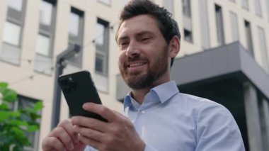 gülümseyen Kafkasyalı orta yaşlı iş adamı erkek işadamı işveren iş adamı şehirdeki ofis binası yakınında cep telefonu uygulaması kullanarak akıllı telefon sohbeti yapan akıllı telefon işi internet kullanan girişimci