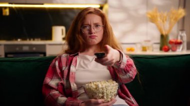 Evde dinlenen genç kız hafta sonu beyaz kadın elinde patlamış mısır kasesiyle kanepede dinleniyor TV programı duygusal tepkisini seçerek sinema dizisini seçiyor.