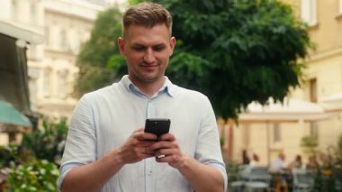 Gülümseyen beyaz adam dışarıda mesaj yazıyor. SMS yazıyor. Açık havada akıllı telefon kullanıyor. Turist turist turist sohbet ediyor, internet bağlantısı kuruyor.