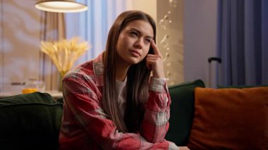 Düşünceli, düşünceli bir kadın kanepenin üzerinde düşünüyor ev sahibi, beyaz, ev sahibi, genç, mutlu, mutlu, düşünceli bir kız. Fikir planı, iç görücü usulü ev kredisi.