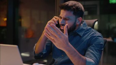 Hintli kızgın iş adamı çığlık çığlığa bağırıyor ofiste gece geç saatlerde konuşan cep telefonu erkek Arap iş adamı girişimci arıyor akıllı telefon sorunu tartışma tartışması laptop çalışıyor