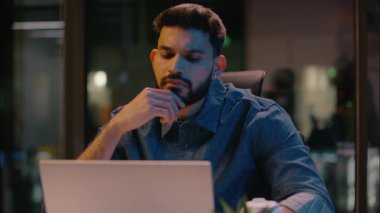Düşünceli Hintli iş adamı, iş adamı, ofis müdürü, işveren Arap erkek CEO, gece geç saatlere kadar çalışıp bilgisayar ticareti yapıyor.