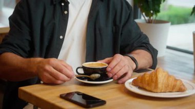 Kafkasyalı mutlu, gülümseyen bir erkek kahvesini yudumluyor rahatlamış iş adamı kafeteryadaki restoran aromalı kafeterya kahvaltı kruvasanı ziyaretçi yemeği ısmarlıyor ev içi içecek müşterisi