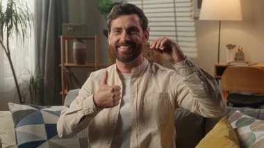 Yeni evin anahtarlarını gösteren mutlu beyaz adam ilk daire satın alan gülümseyen erkek ev sahibi ev yatırım evi ipoteği konut kirası taşınma günü banka kredisi satın alma başparmağı