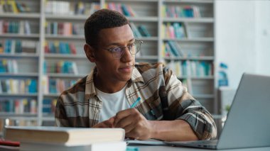 Bilgisayarda bilgisayar eğitimi alan Afrikalı Amerikalı bir adam. Erkek öğrenci, not defteri kopyalıyor. Sınav görevlisi, kütüphane teknolojisi diploması hazırlıyor.
