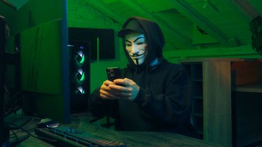 Lviv, Ukrayna - 3 Haziran 2024: Anonim hacker akıllı telefon bilgisayar teknolojisi bilgisayar teknolojisi hırsızı maskeli adam tehlikesi parmakla göstererek dolandırıcılık, internet yazılımı saldırısı virüsü