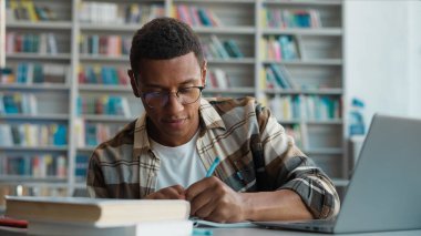 Bilgisayarda bilgisayar eğitimi alan Afrikalı Amerikalı bir adam. Erkek öğrenci, not defteri kopyalıyor. Sınav görevlisi, kütüphane teknolojisi diploması hazırlıyor.
