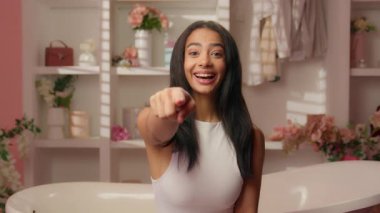 Neşeli, pembe banyodaki neşeli, mutlu, mutlu, gülümseyen İspanyol kız. Kamerayı işaret eden kız. Seni buraya davet ediyorum.