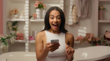 İspanyol kadın güzel kız, gülümseyen kadın tüketici banyodaki güzellik müşterisi akıllı telefon siparişi internet alışveriş uygulaması internet alışverişi kozmetik krom anahtar yeşil ekran cep telefonu satın al