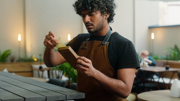 Upset sad Indian Arabian latino man waiter in apron guy cleaner cafe worker male business owner barista serving in cafe no money cash tips bad service in restaurant bill payment dissatisfied worried