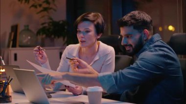 Çok ırklı takım çalışması yapan Hintli erkek Kafkas kadın iş ortağı iş arkadaşları karanlık gece ofis kızı erkek işadamı iş kadını tasarımcılar proje dizüstü bilgisayarlarını tartıştılar