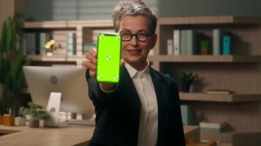 Orta yaşlı Avrupalı iş kadını cep telefonu web akıllı telefon yeşil ekran krom anahtar fotokopi alanı gösteriyor. Uygulamada yetişkin kadın işveren gibi başparmağınızı kaldırın.