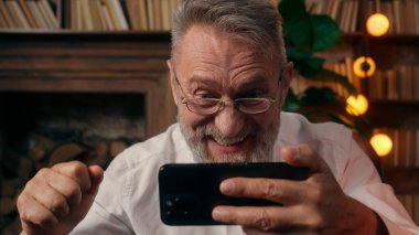 Heyecanlı, Kafkasyalı, elinde cep telefonu olan yaşlı, akıllı erkek, yaşlı, şaşırmış ofis bahsini kazan, zafer kazan, online kumar işi yap.