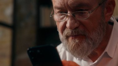 Kafkasyalı bir adam cep telefonu kullanıyor, akıllı telefon kullanıyor, internetten sohbet ediyor, mesajlaşıyor, mutlu, yaşlı, yaşlı, gülümseyen iş adamları, ev içi web gözlükleri takıyor.