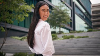 Arkadan bakıldığında başarılı Asyalı Çinli kadın iş kadını gülümsüyor profesyonel çalışan kız başını çevirip kameraya bakıyor şehir yöneticisinin merdivenlerinden dışarı çıkıyor.