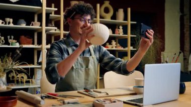 Beyaz adam çömlekçi sanat heykeltraşı çömlek atölyesinde küçük işletme sahibi gülümseyen adam satış elemanı el yapımı kase dükkanı satıyor seramik video blogu, cep telefonu kameraları, sosyal medya