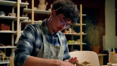 Konsantre erkek çömlekçi heykeltraş erkek Kafkasyalı erkek tasarımcı çömlekçilik atölyesinde ustalaşmış el yapımı masa başı el işi seramik hobisi üzerinde merdane ile kil modelliği yapıyor.