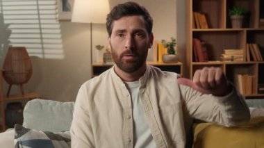 Üzgün, asık suratlı, beyaz, erkek, kanepede oturan, el hareketlerini beğenmeyen, el hareketlerini beğenmeyen, memnun olmayan, kameraya bakmaktan hoşlanmayan adam.