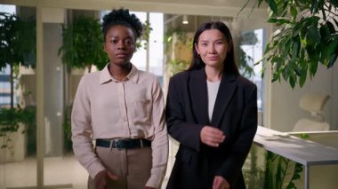 İki kendine güvenen iş kadını çok ırklı Afrikalı kızlar ofiste yan yana poz veren Çinli Amerikalı iş ortakları profesyonel iş arkadaşları iş arkadaşları.