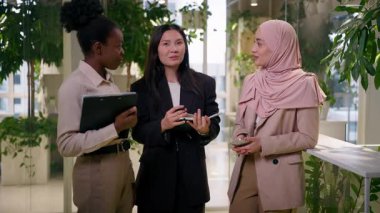Çok ırklı kızlar, ofisteki üç kadın, Afrikalı Asyalı iş kadını iş arkadaşları, gülümseyen mutlu iş arkadaşları, konuşan Müslüman meslektaşlar.