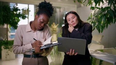 Çok görevli ofis iş arkadaşları, çeşitli iş kadınları, Afrikalı Asyalı iş arkadaşları, iş kadınları, takım çalışması, çalışanların iş birliği yapması, notlar yazması, dizüstü bilgisayarla ilgili görevler.