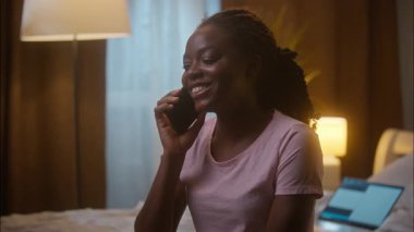 Gülen, Afro-Amerikalı, etnik kadın, cep telefonuyla konuşan, cep telefonu sohbeti yapan, akıllı telefon konuşmaları, dedikodu yapan, yatak odasında, gece geç saatlerde yatak odasında oturan arkadaşlar.